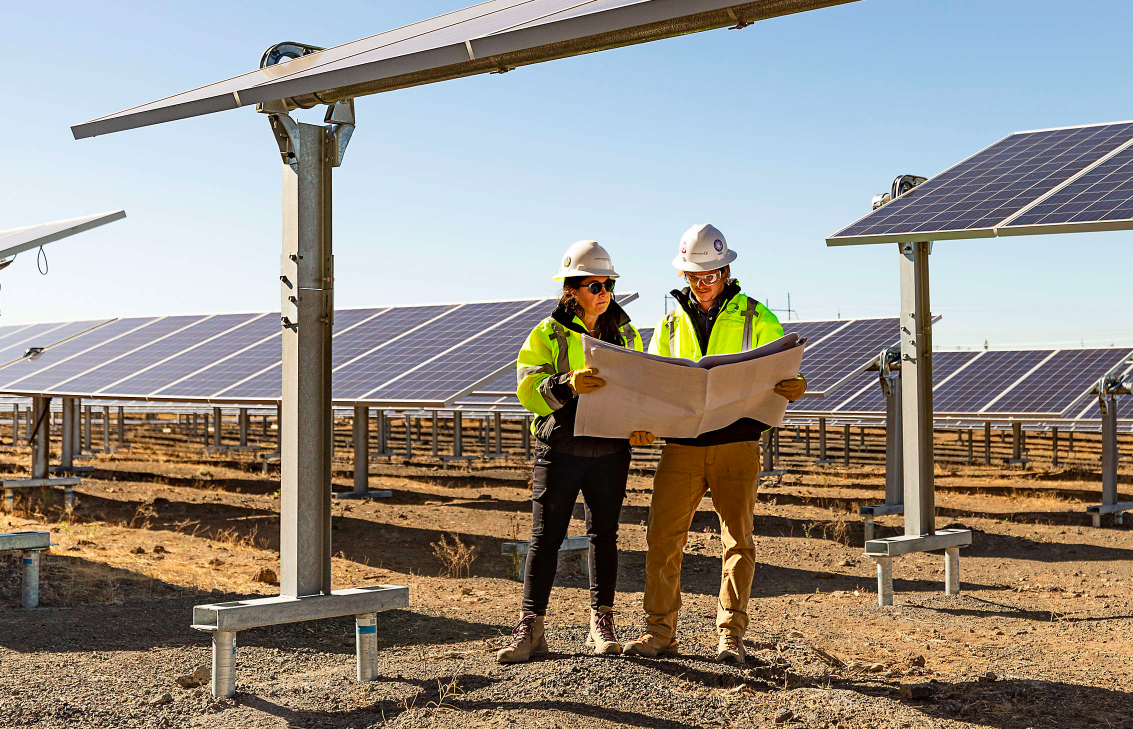 A man and woman reading blue prints in a solar panel field